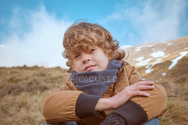 Rapaz bonito sentado na colina perto do riacho — Fotografia de Stock