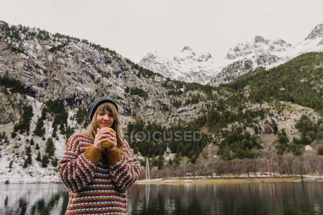 Jeune femme assise sur un banc les yeux fermés près d'une vue imprenable sur la surface de l'eau entre de hautes montagnes avec des arbres dans la neige dans les Pyrénées — Photo de stock