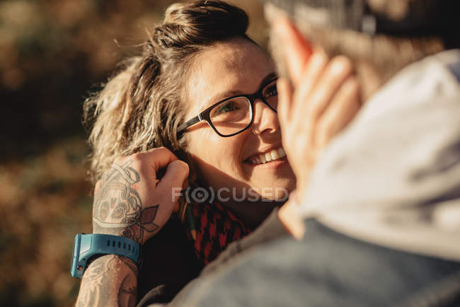 Bearded man embracing cheerful woman near wood in forest on blurred background — Stock Photo