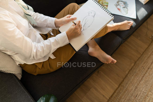 Mulher desenhando em papel no sofá no quarto — Fotografia de Stock