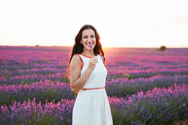 Sorridente giovane donna in abito che mostra fiori tra campo viola lavanda — Foto stock