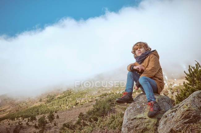 Boy sitting near hill on foggy day — Stock Photo