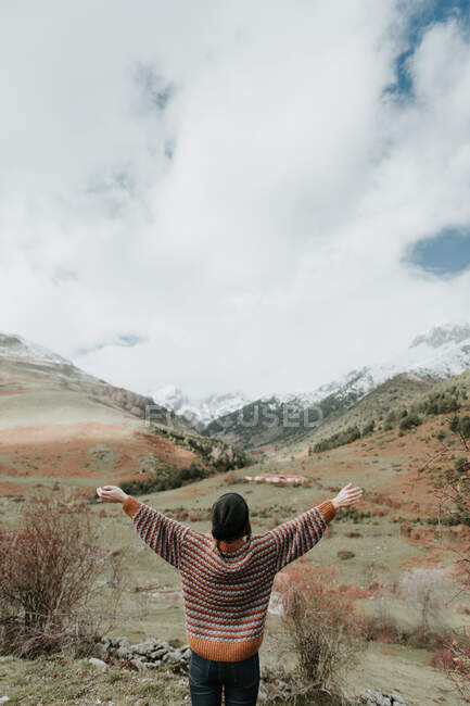 Rückenansicht einer jungen Dame in Pullover und Hut, die in einer wunderschönen Landschaft zwischen Bergen steht und die Arme in die Höhe reckt. — Stockfoto