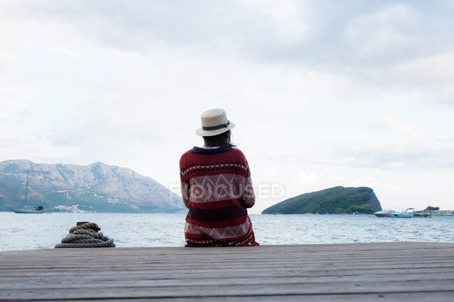 Anonymous woman in hat sitting on pier — Stock Photo