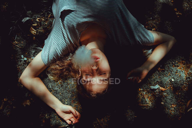 Von oben junge Frau mit geschlossenen Augen, die im Sommer auf dem Boden raucht — Stockfoto