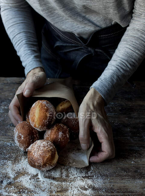 Урожай людини тримає набір свіжих тортів з цукровою пудрою на дерев'яному столі в темряві — стокове фото