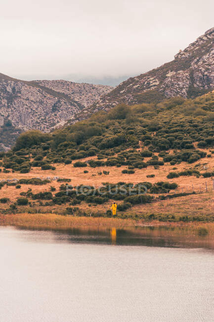 Person in gelbem Regenmantel am Ufer des Sees in der Nähe eines Berges in Isoba, Kastilien und León, Spanien — Stockfoto