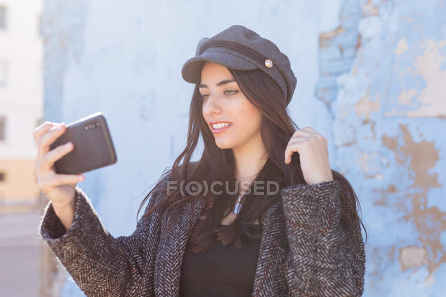Charmante dame hispanique prenant selfie avec téléphone portable devant un mur minable — Photo de stock