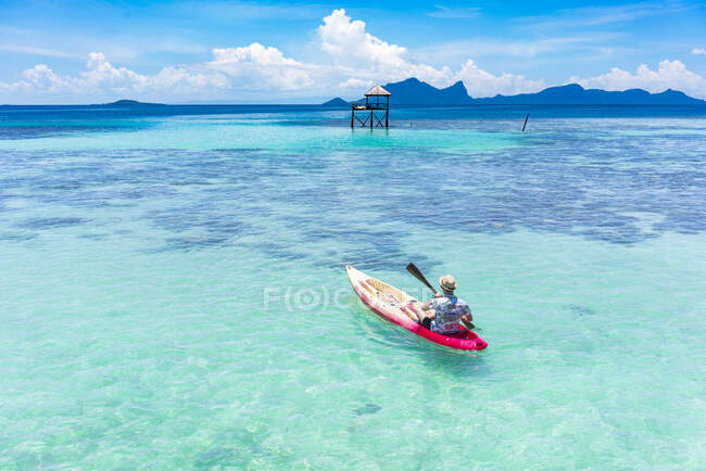 Вид сзади мужская лодка на каноэ с веслом на удивительное лазурное море и голубое небо в Малайзии — стоковое фото