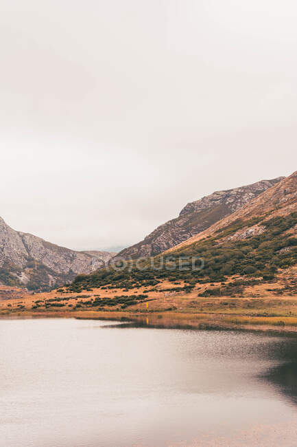 Persona in impermeabile giallo che va sulla riva del lago vicino a wigwam e collina in Isoba, Castiglia e Leon, Spagna — Foto stock