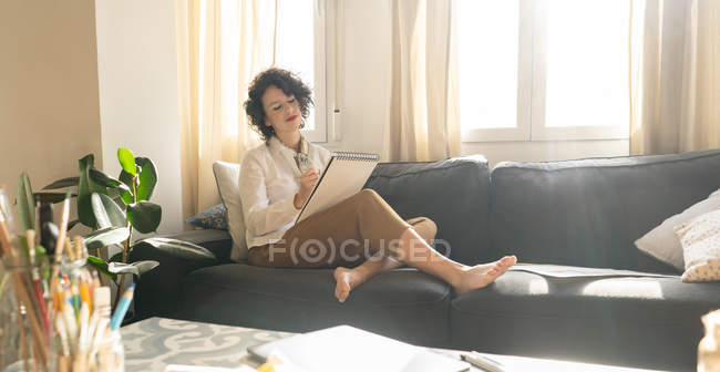 Жінка малює на папері на дивані в кімнаті. — стокове фото