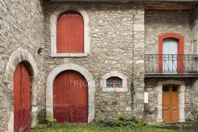 Patio con césped verde entre la antigua casa de piedra gris con puertas rojas en los Pirineos - foto de stock