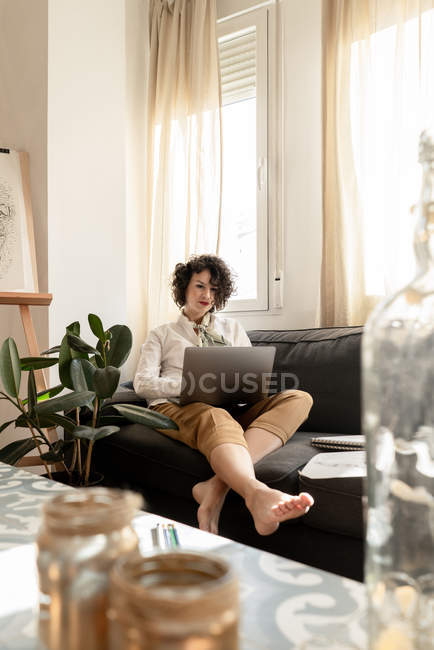 Donna che utilizza il computer portatile vicino disegna su carte sul divano in camera — Foto stock