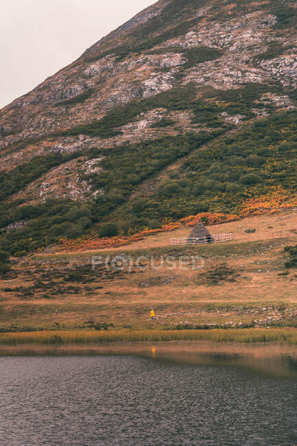 Pessoa de capa de chuva amarela que vai à margem do lago perto de wigwam e colina em Isoba, Castela e Leão, Espanha — Fotografia de Stock