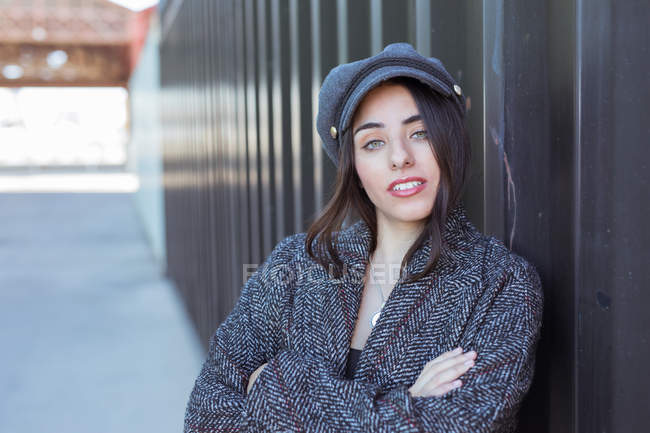 Portrait of young Hispanic lady leaning on metal wall with crossed arms — Stock Photo