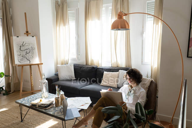 Женщина рисует на бумаге на диване в комнате — стоковое фото