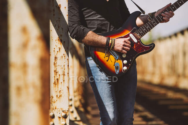 Culture Homme adulte avec guitare électrique debout sur le pont altérée par une journée ensoleillée à la campagne — Photo de stock