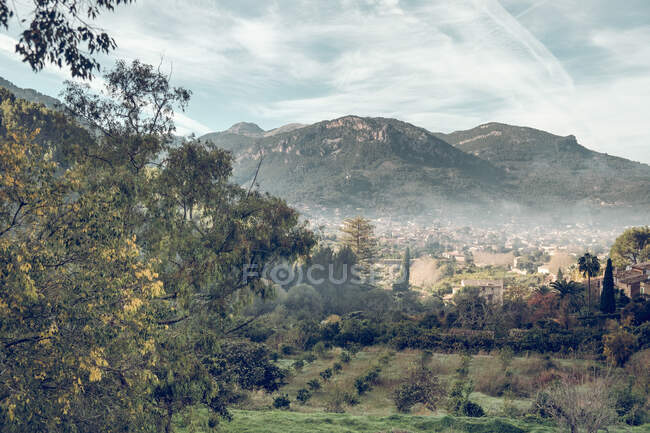 Picturesque drone view of wonderful green trees and old small town near amazing mountain ridge on cloudy day — Stock Photo