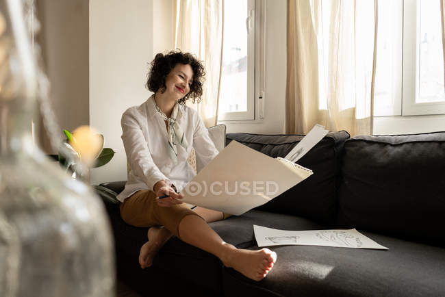 Donna che disegna su carte sul divano in camera — Foto stock