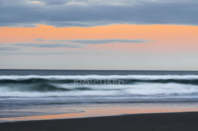Pintoresco paisaje de costa tranquila con grandes olas en larga exposición corriendo en la playa contra el cielo crepuscular - foto de stock