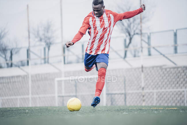 Afrikanischer Fußballer mit rot-weißer Ausrüstung beim Fußballspielen. — Stockfoto