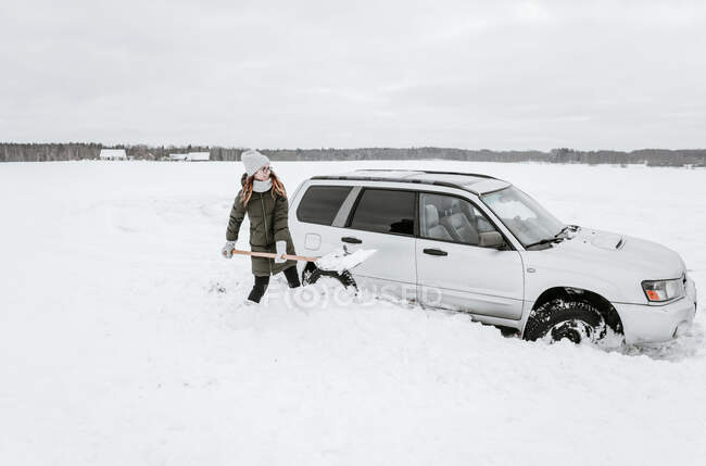 Jovencita con pala excavando nieve del automóvil cerca del prado en Vilna, Lituania - foto de stock