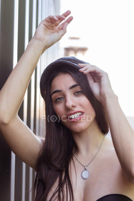Appassionato giovane donna in alto tenendo tappo sulla testa e guardando la fotocamera su sfondo sfocato — Foto stock