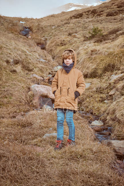 Carino ragazzo in piedi su collina vicino ruscello — Foto stock