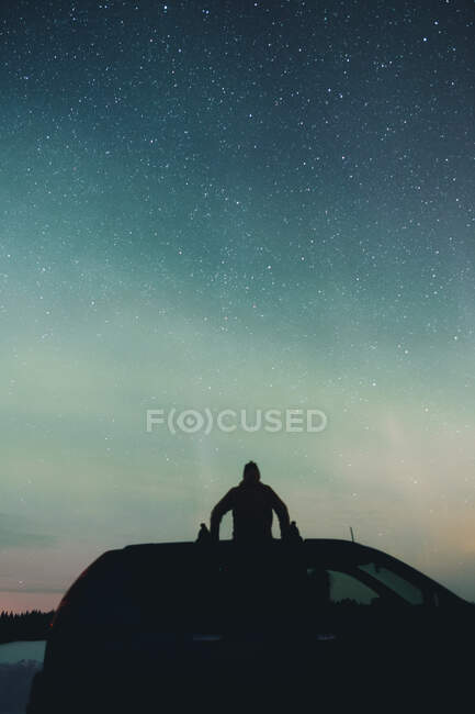 Silhouette of unrecognizable male on top of modern car against magnificent night sky in Arctic countryside — Stock Photo