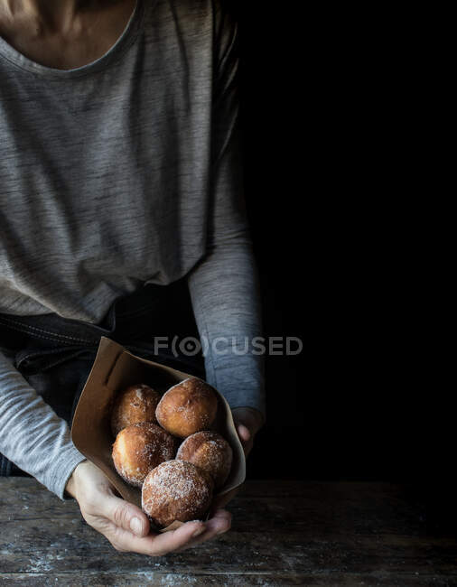 Crop human holding a set of fresh cakes with powdered sugar on wooden table in darkness — Stock Photo