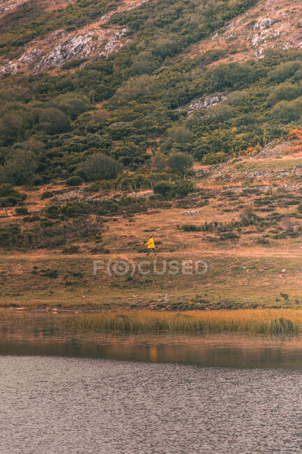 Persona en impermeable amarillo que va a la orilla del lago cerca de Wigwam y colina en Isoba, Castilla y León, España - foto de stock
