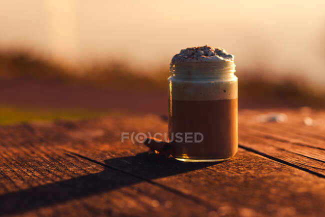 Paus de canela aromáticos perto de jarro de café gostoso com creme na mesa de madeira serrada — Fotografia de Stock