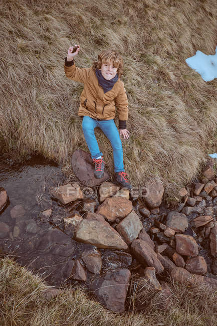 Мальчик, сидящий на траве возле ручья — стоковое фото
