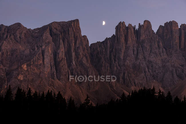 Red rocky mountain peaks at moon rise time over twilight sky. Dolomites Alps, Italy — Stock Photo