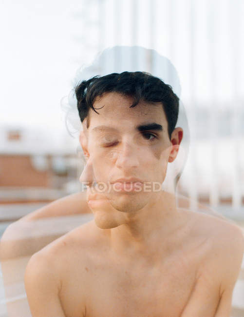 Dupla exposição do jovem homem sem camisa olhando para a câmera e sentado na varanda no fundo borrado — Fotografia de Stock
