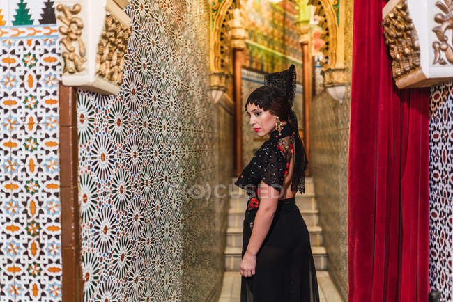 Side view of passionate young woman in dress standing in narrow corridor decorated by mosaic — Stock Photo