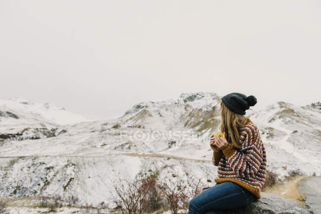 Vista lateral da jovem senhora em suéter e chapéu segurando caneca e olhando para colinas na neve em Pirinéus — Fotografia de Stock