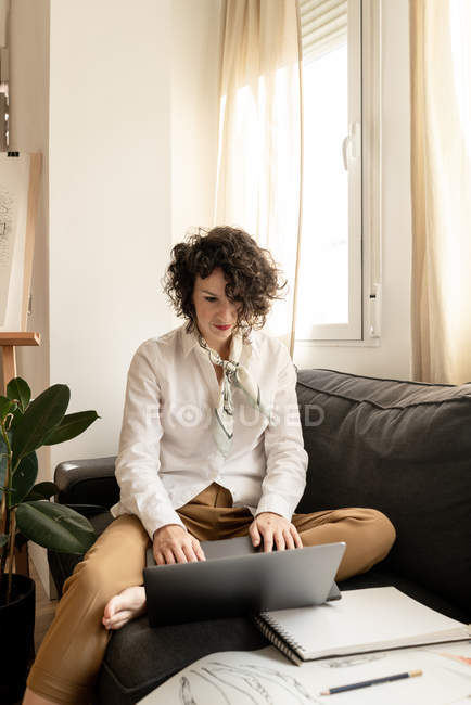 Женщина с ноутбуком рядом рисует на бумаге на диване в комнате — стоковое фото