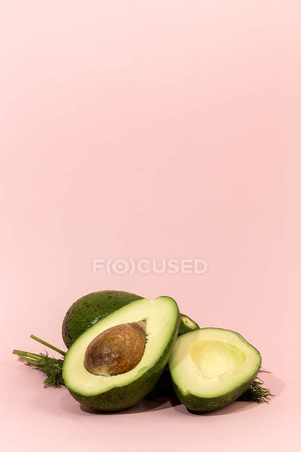 Avocado fresco intero e dimezzato su sfondo rosa — Foto stock