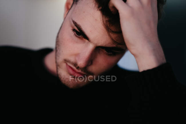 Gros plan jeune homme réfléchi en pull noir avec la main sur les cheveux regardant en bas à Madrid, Espagne — Photo de stock
