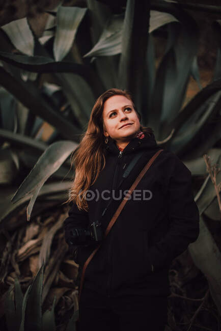 Femme en manteau avec caméra près des plantes — Photo de stock