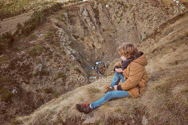 Cute boy sitting on hill near brook — Stock Photo