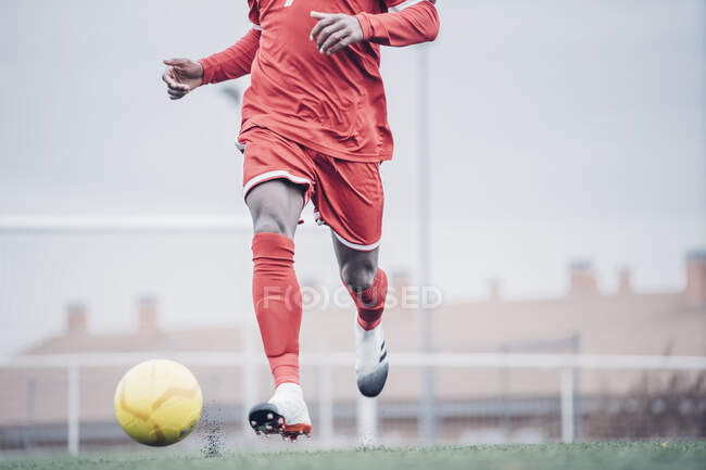 Afrikanischer Fußballer mit rotem Outfit beim Fußballspielen. — Stockfoto