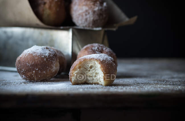 Bitten cake near set of baked loaf with powdered sugar on table in darkness — Stock Photo