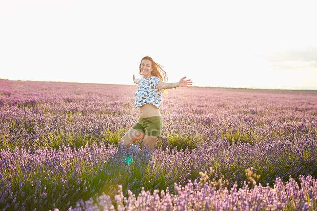 Молодая женщина бежит между фиолетовым лавандовым полем на закате — стоковое фото