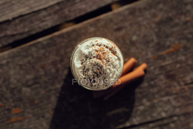 Palitos aromáticos de canela cerca del frasco de delicioso café con crema en la mesa de madera - foto de stock