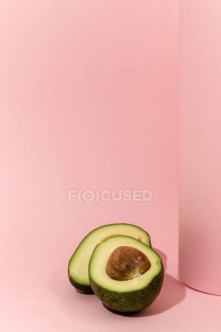 Abacate fresco cortado pela metade sobre fundo rosa — Fotografia de Stock