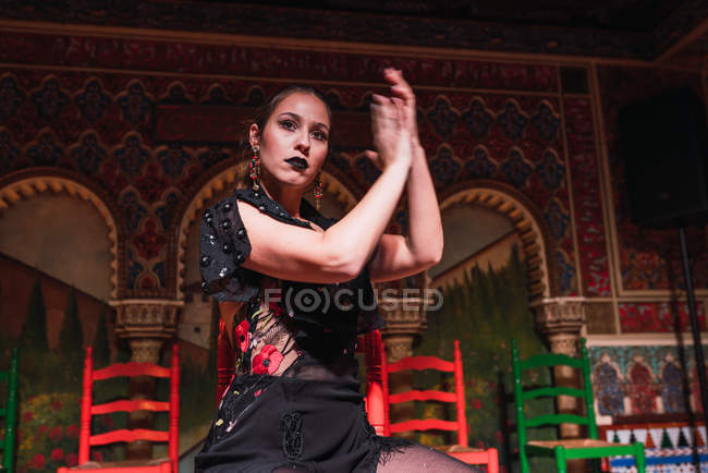 Девушка в платье хлопает в ладоши и танцует на сцене возле стульев в роскошной комнате, украшенной мозаикой — стоковое фото