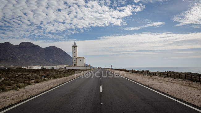 Tower building and majestic mountain near asphalt countryside road on cloudy day — Stock Photo
