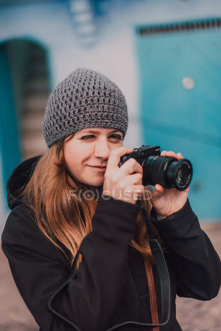 Young photographer woman winking and standing on street while setting camera in Chefchaouen, Morocco — Stock Photo